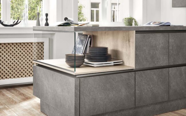 Close-up of a StoneArt kitchen island featuring Taupe Grey Basalt reproduction cabinetry with a synchronized pore finish. The design includes integrated shelving with wooden accents, creating a harmonious blend of urban and homely aesthetics. This setup showcases the realistic stone look and modern functionality, perfect for German kitchens at trade prices.